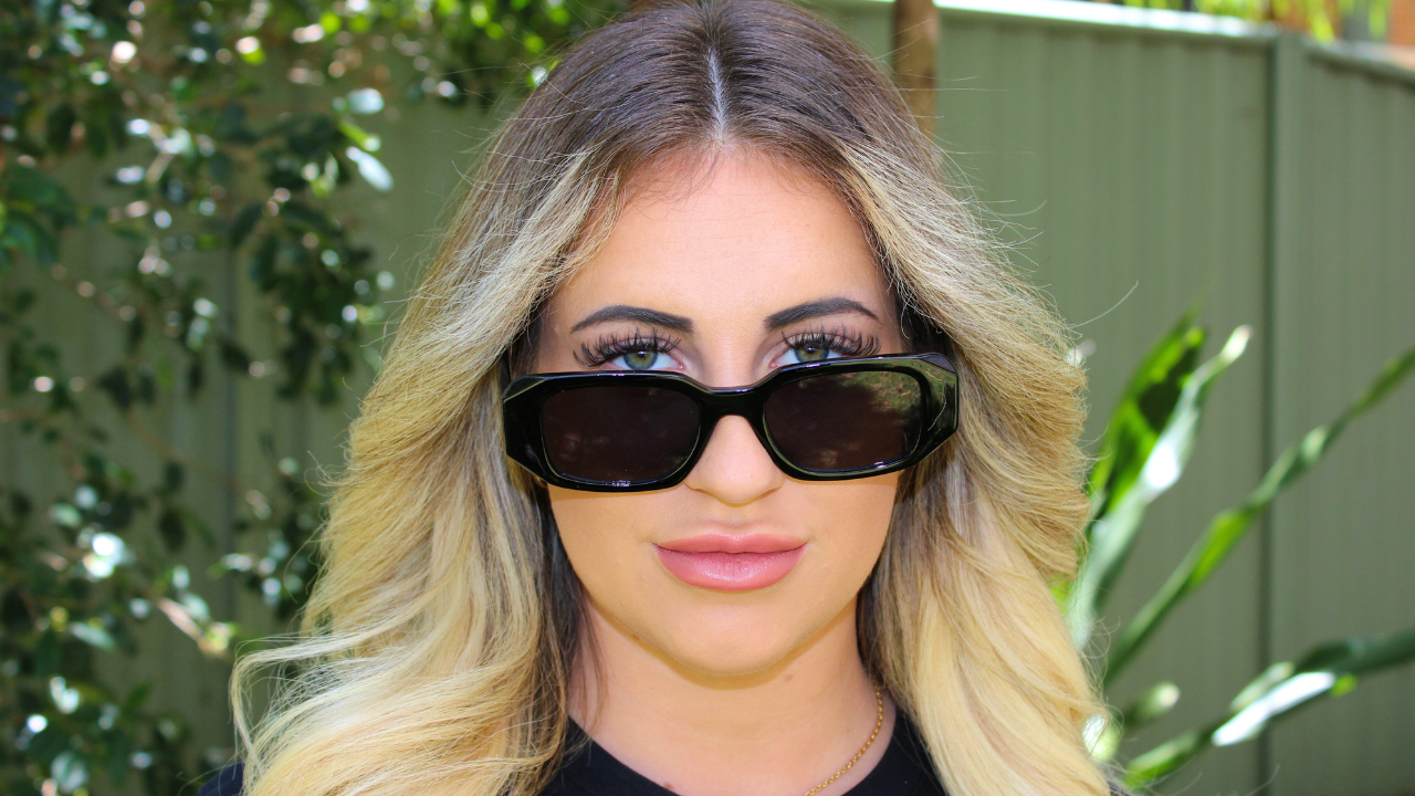 Woman wearing black rectangular sunglasses outdoors with soft natural lighting